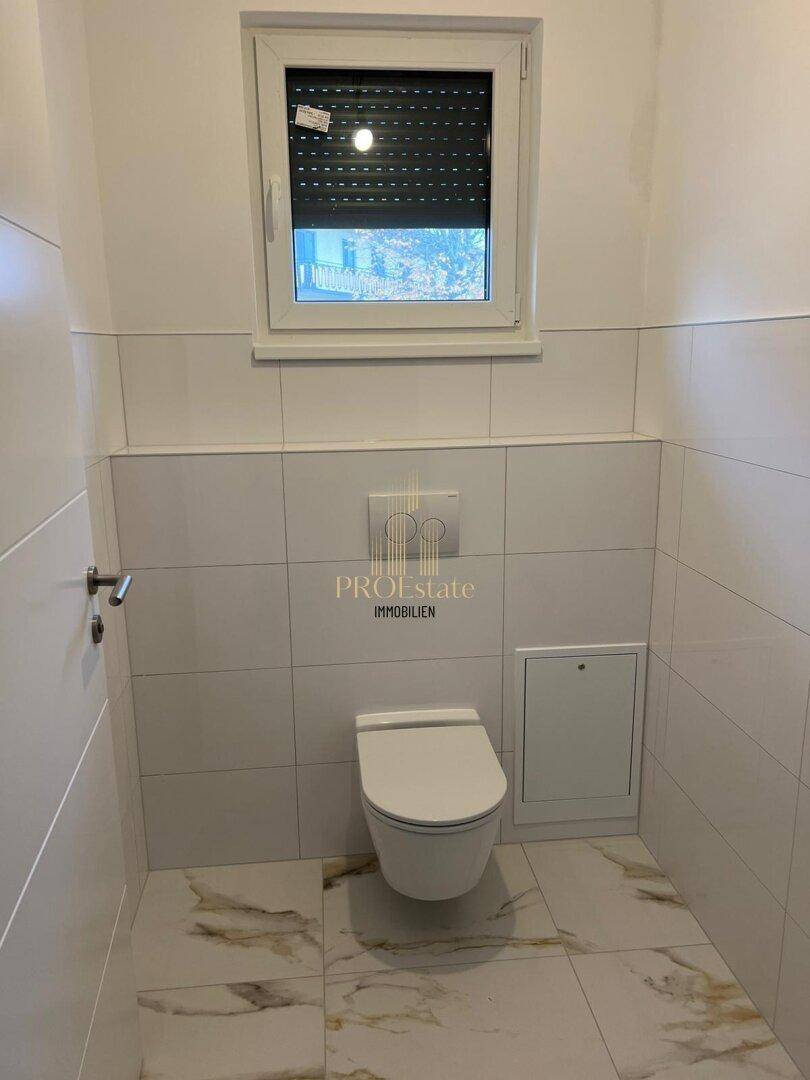 Modernes Gäste-WC mit weißen Fliesen, wandhängendem WC und Fenster mit Rollladen.