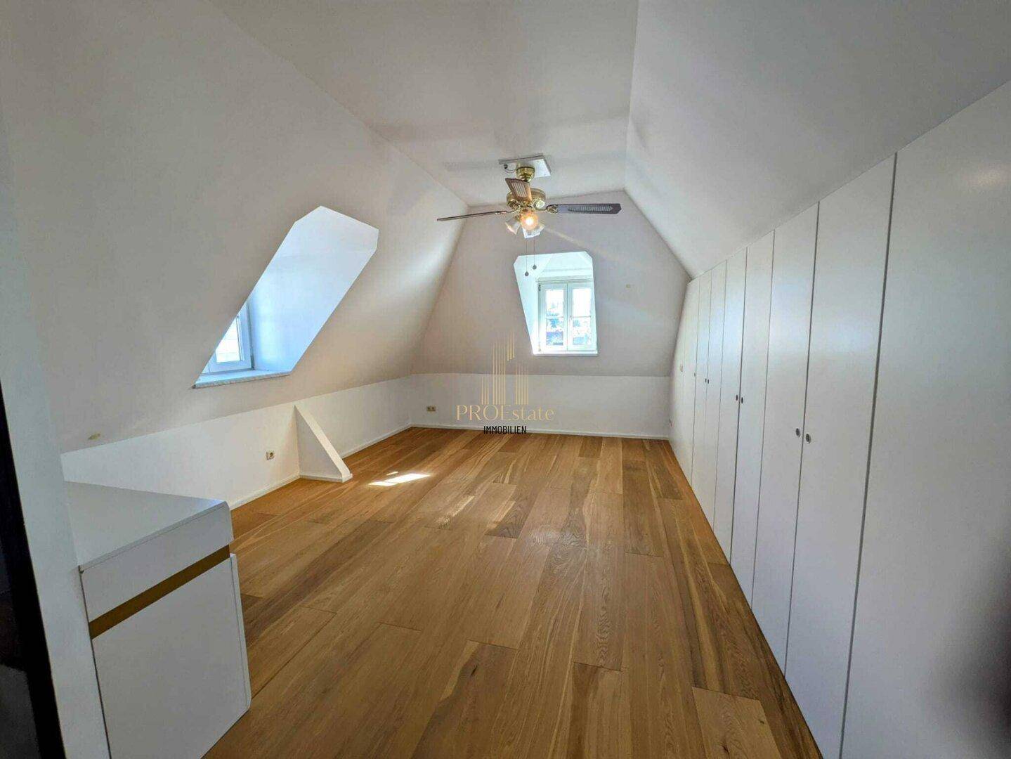 Geräumiges Dachzimmer mit Holzboden, Dachschrägen und integrierten Wandschränken.