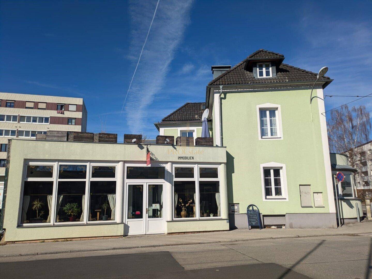 Gebäudeansicht von der Straße mit hellgrüner Fassade und großen Fenstern im Erdgeschoss.