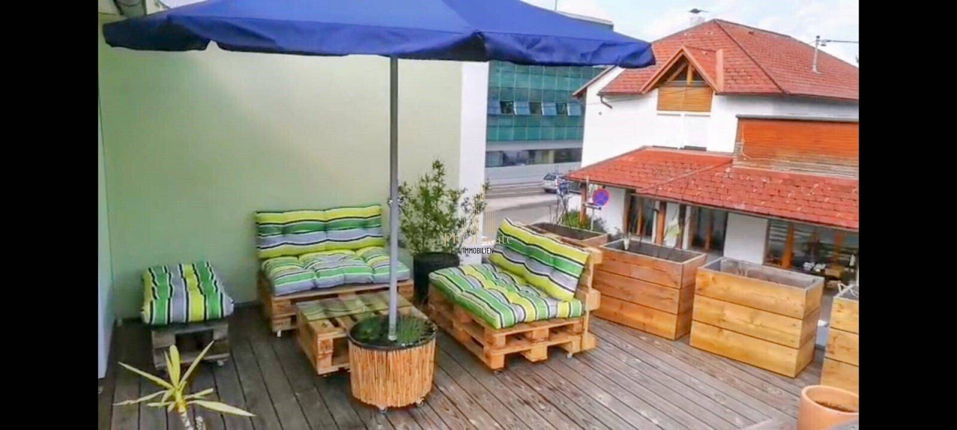 Dachterrasse mit Palettenmöbeln, Sonnenschirm und Blick auf die Umgebung.
