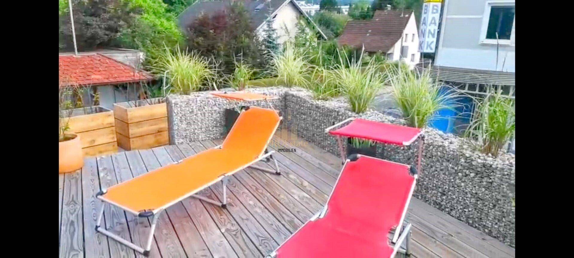 Sonniger Dachgarten mit Liegestühlen, Gabionen und Pflanzen für Entspannung im Freien.