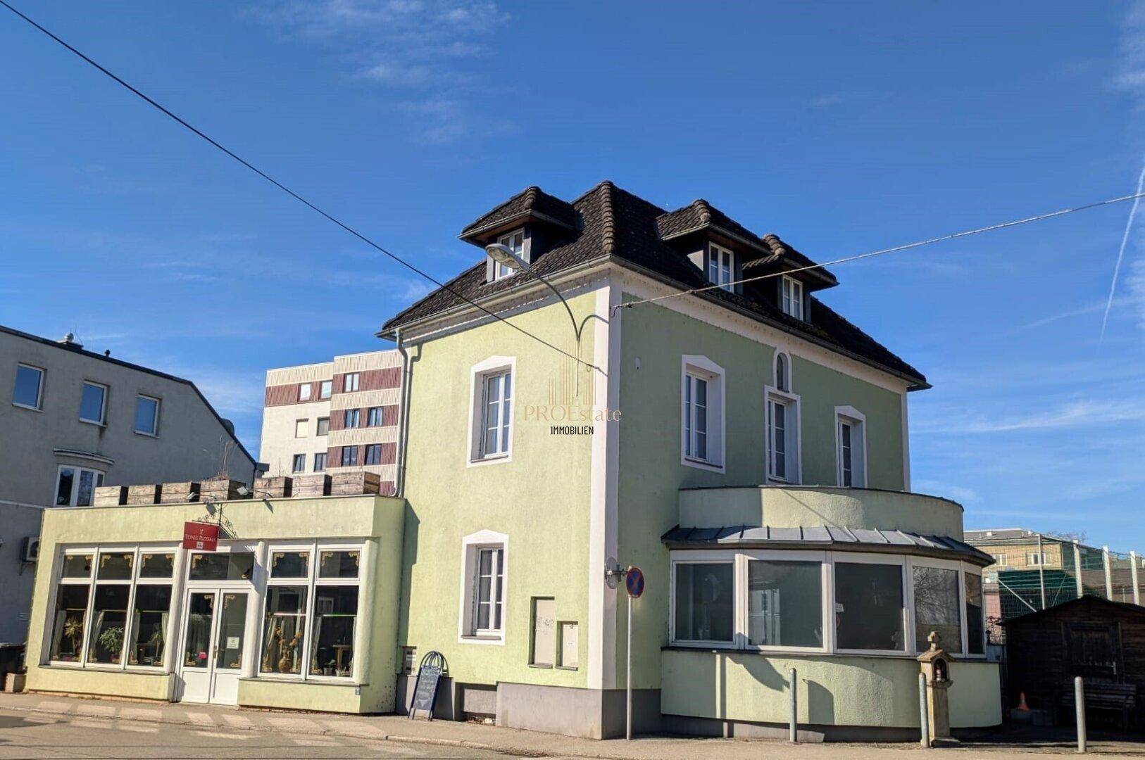 Historisches Gebäude mit hellgrüner Fassade und Mansarddach in städtischer Umgebung.