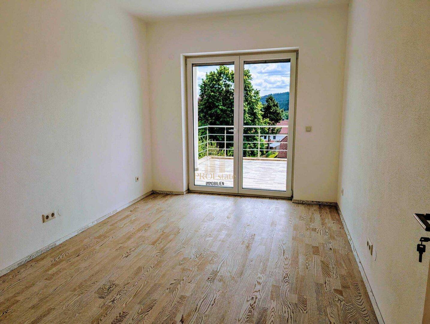 Helles, leeres Zimmer mit Holzboden und Zugang zu einer großen Terrasse mit Weitblick.