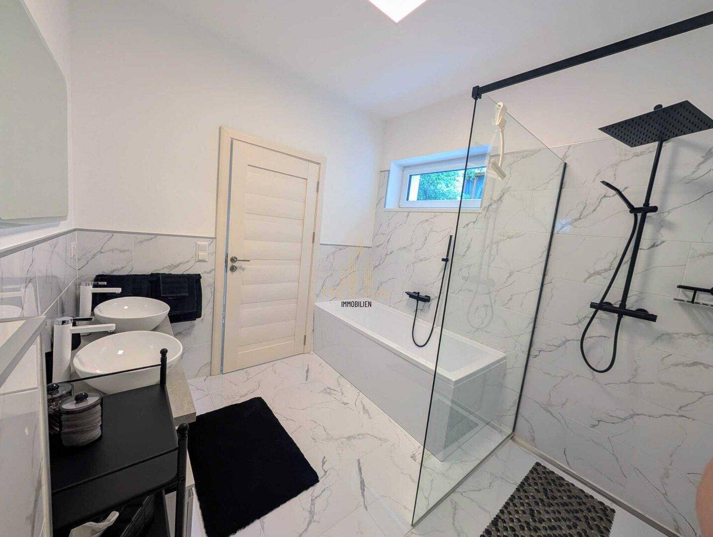 Modernes Badezimmer mit weißen Marmorfliesen, zwei Aufsatzwaschbecken und einer Badewanne mit Dusche.