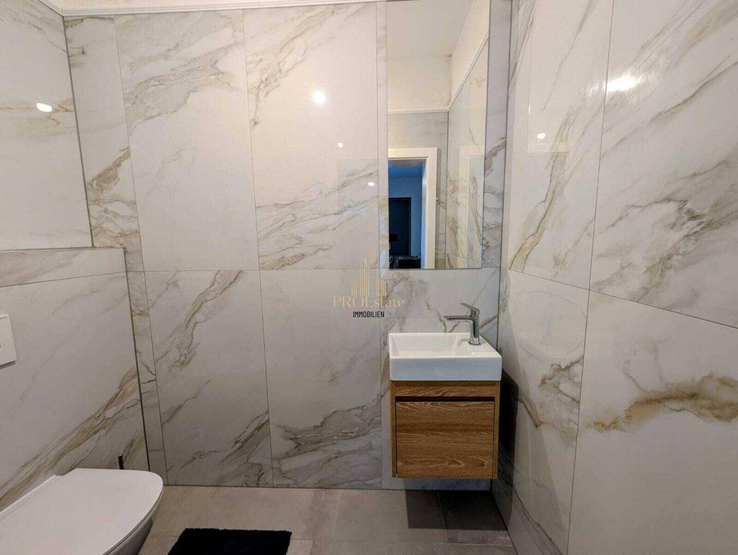 Modernes Badezimmer mit Marmoroptik-Fliesen, Einzelwaschbecken und Wand-WC.
