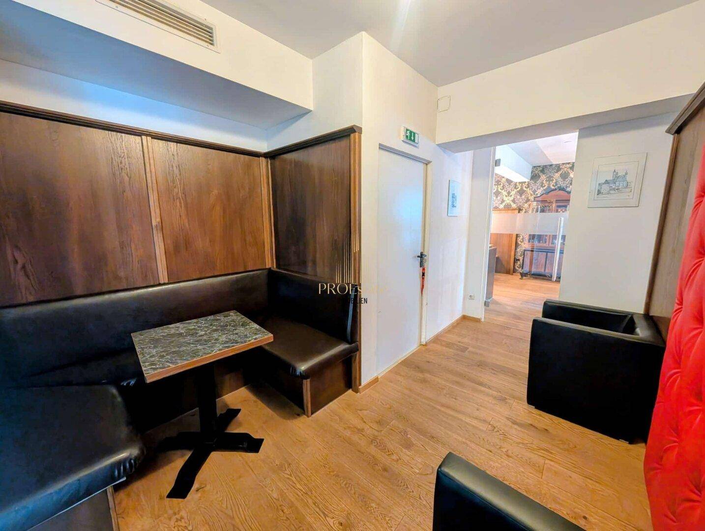 Ein weiterer Bereich des Restaurants mit bequemen Sitzbänken, Holztischen und einem Durchgang zu anderen Räumen.
