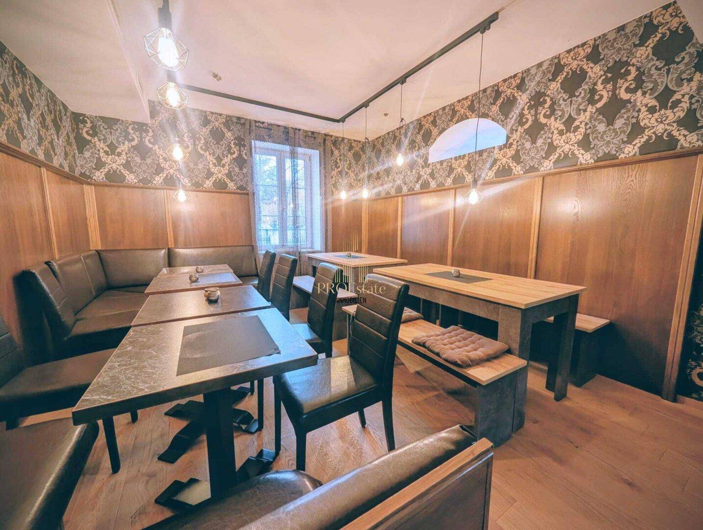 Geräumiger Restaurantbereich mit vielfältigen Sitzmöglichkeiten, dunkler Tapete und warmen Holzelementen, gut beleuchtet.