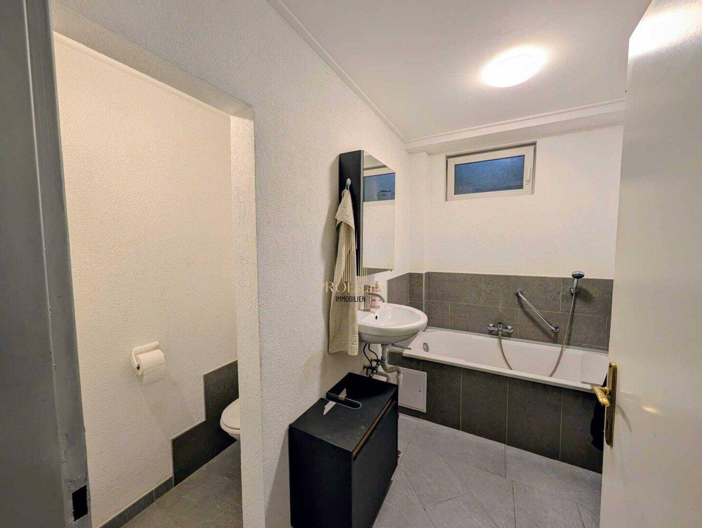 Einfaches Badezimmer mit Badewanne, Waschbecken und separatem WC-Bereich.