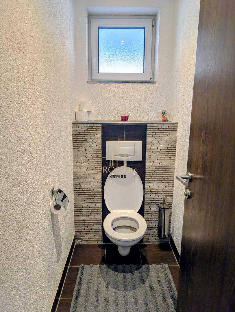 Kleines Gäste-WC mit Fenster, Wand-WC und dekorativer Steinwand.
