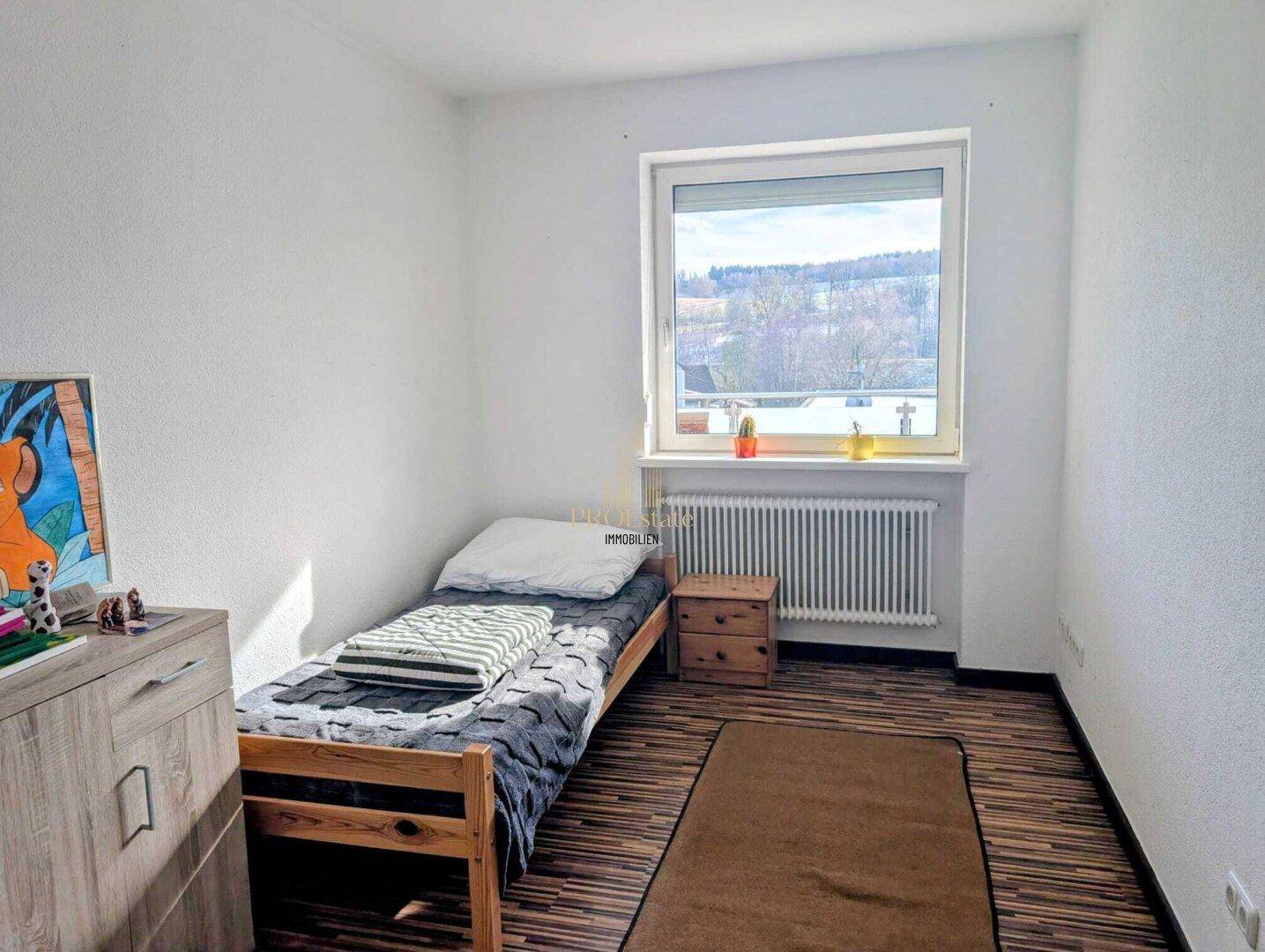 Helles Schlafzimmer mit Einzelbett, Holzboden und Fenster mit Ausblick.