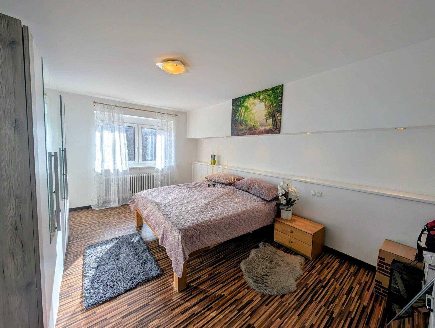 Geräumiges Schlafzimmer mit Doppelbett, Holzboden und großen Fenstern.