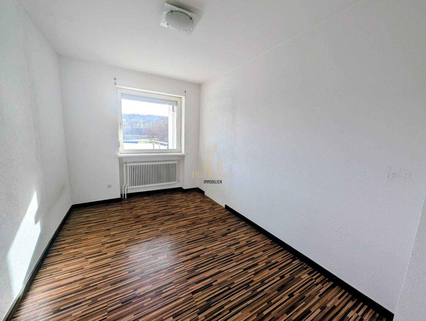 Leeres Schlafzimmer mit Holzboden und großem Fenster, bereit zur individuellen Gestaltung.