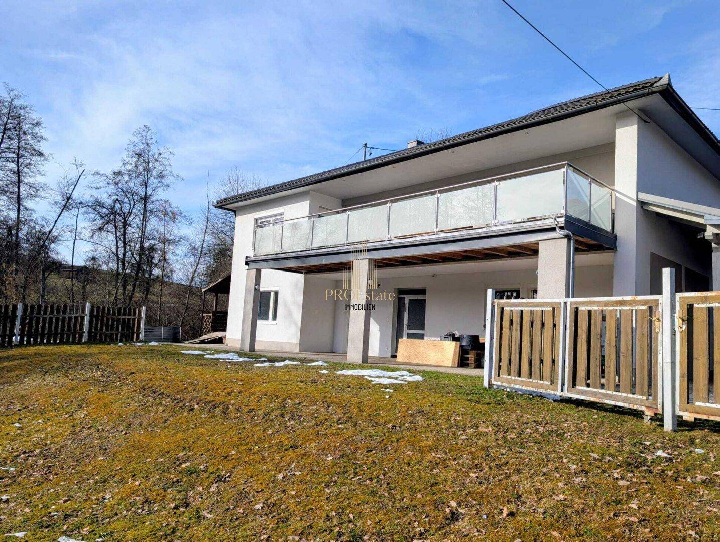 Modernes Wohnhaus mit Balkon und Gartenbereich, umgeben von Natur und leichtem Schneefall.