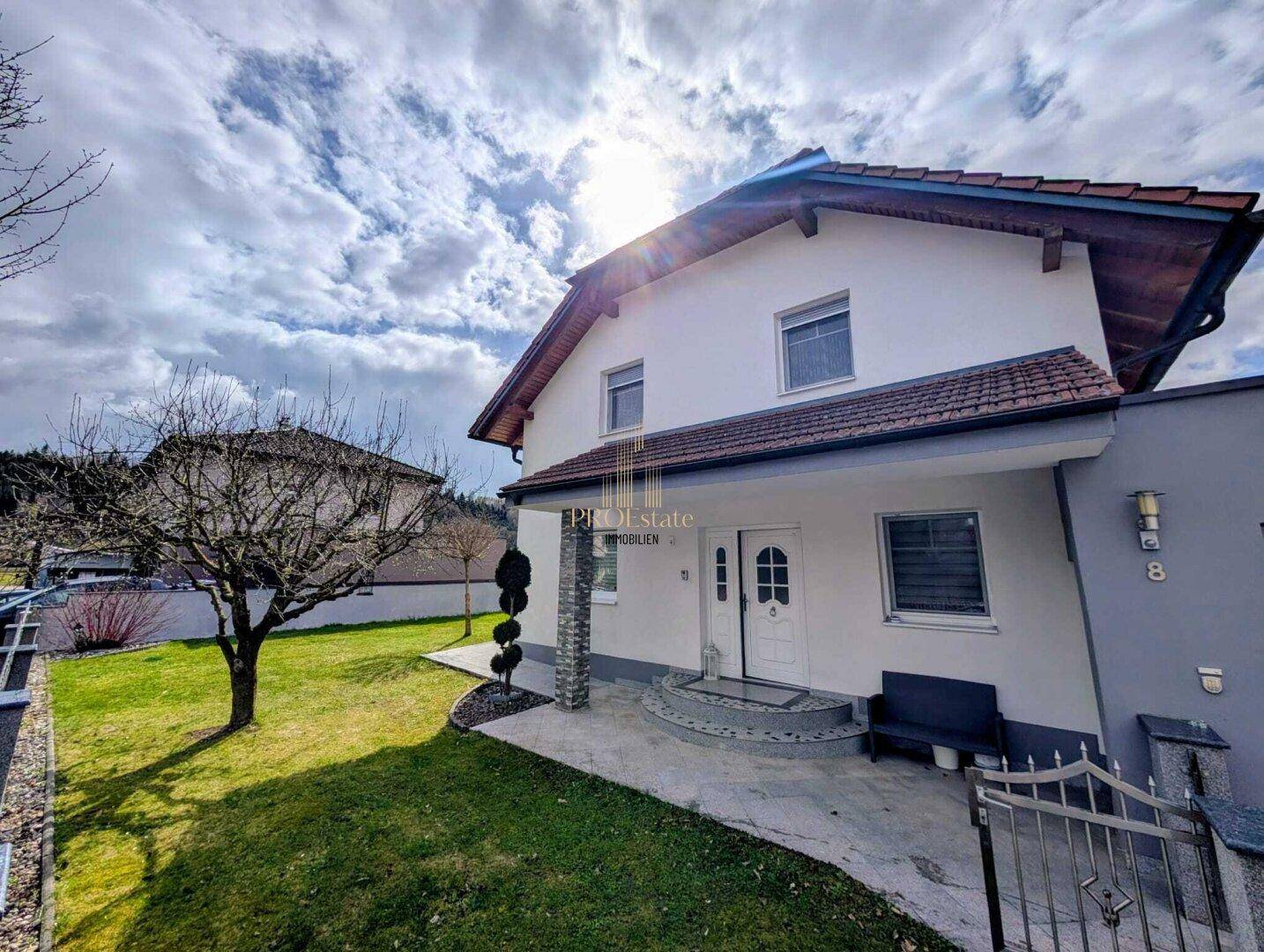 Eingangsbereich eines modernen Einfamilienhauses mit gepflegtem Vorgarten und sonnigem Ambiente.