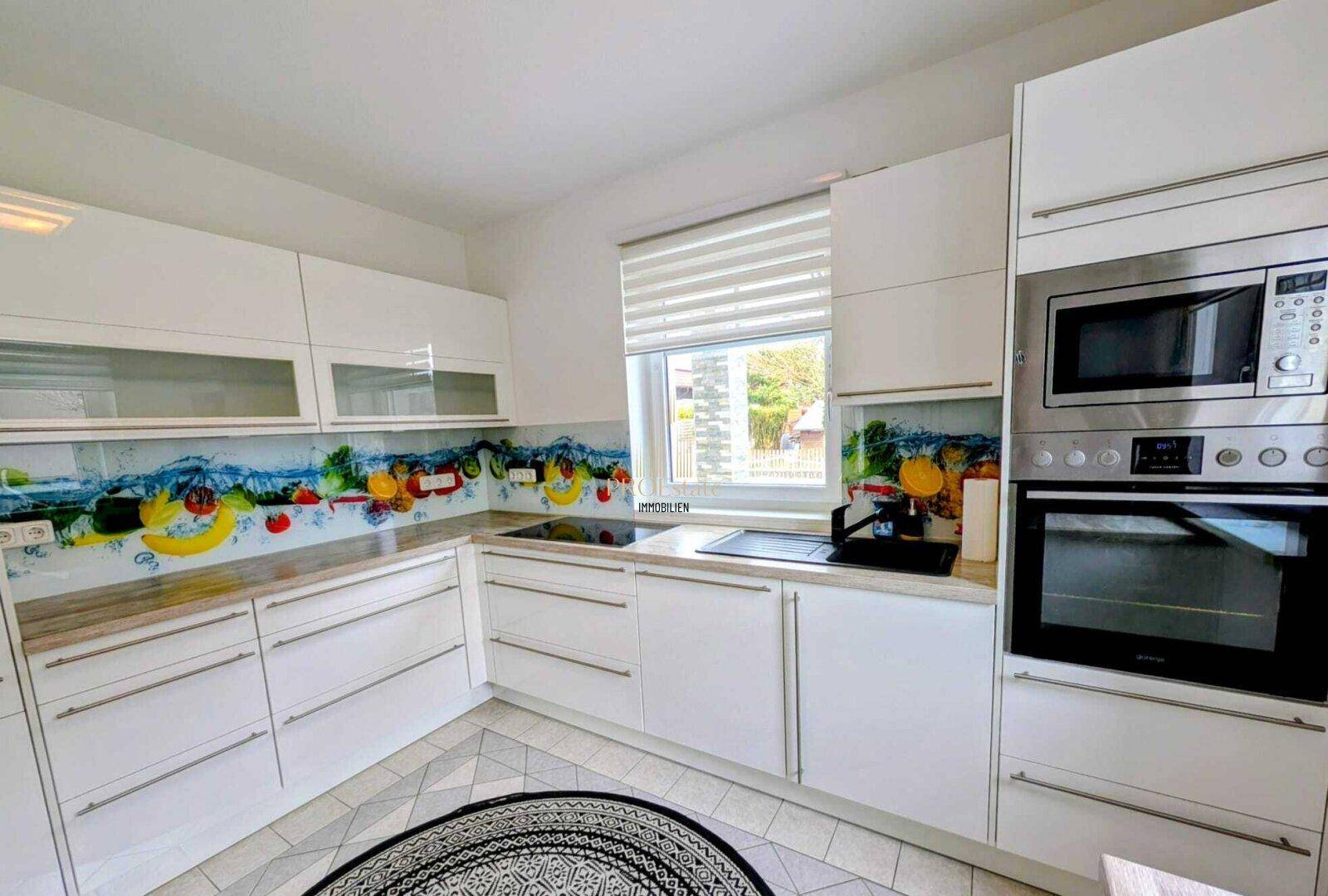 Moderne Küche mit weißen Hochglanzfronten, integrierten Geräten und farbenfroher Rückwand.