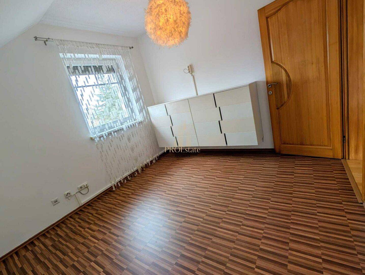 Helles Schlafzimmer mit Laminatboden, Dachschräge und einem Fenster mit Blick nach draußen.