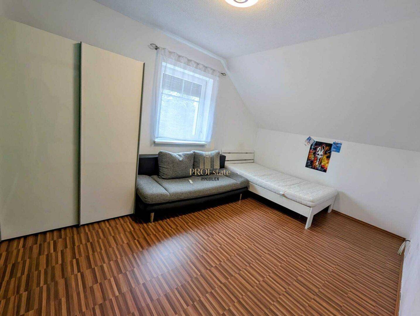 Schlafzimmer mit Laminatboden, Dachschräge und einem Bett sowie einem Sofa.