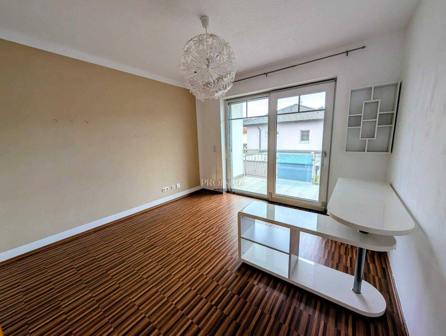Helles Zimmer mit Laminatboden und Schiebetür, die zu einem Außenbereich führt.