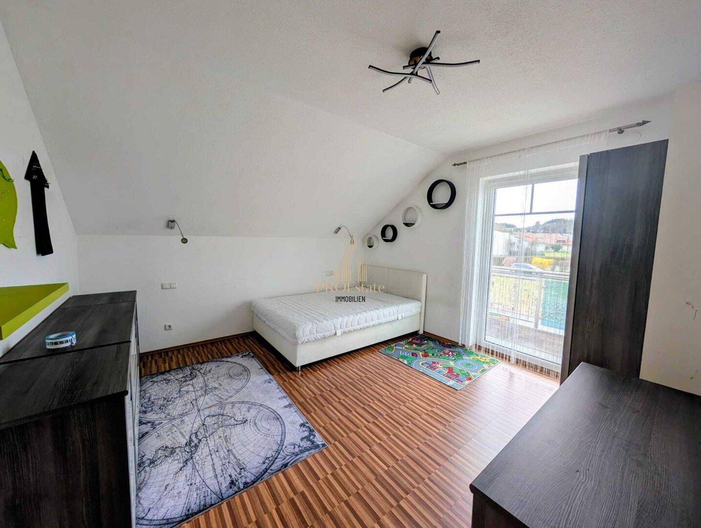 Schlafzimmer im Dachgeschoss mit Laminatboden, Dachschräge und Zugang zu einem Balkon.