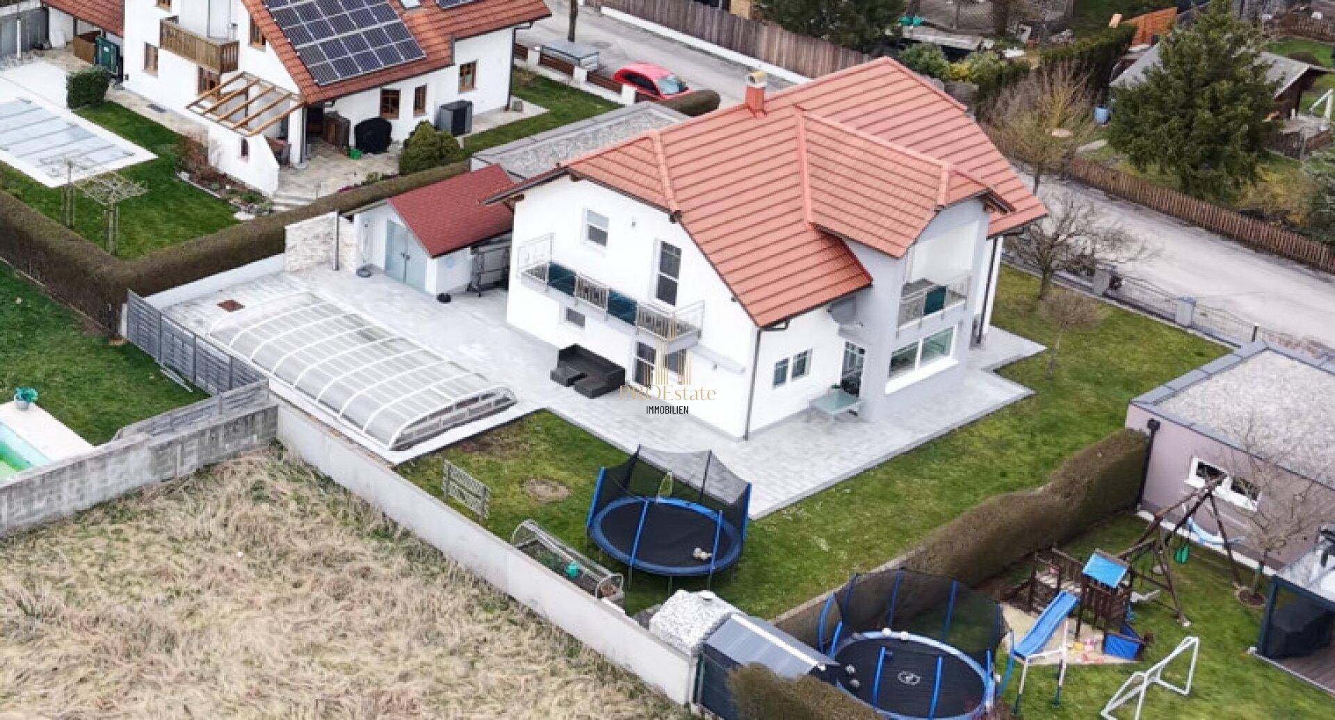 Luftaufnahme des Einfamilienhauses mit großem Garten, Pool und Spielgeräten für Kinder.