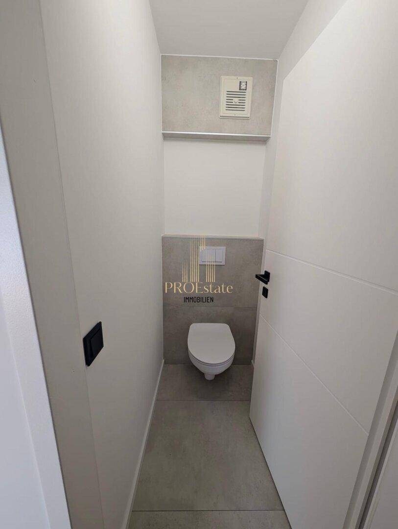 Separates Gäste-WC mit wandhängender Toilette, Fliesen und Abluftsystem, praktisch und platzsparend gestaltet.