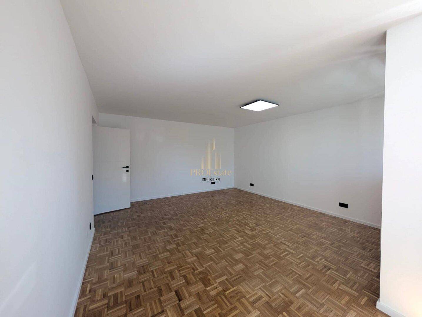 Großes, leeres Wohnzimmer mit Parkettboden und weißen Wänden, bereit zur Einrichtung und individuellen Gestaltung.