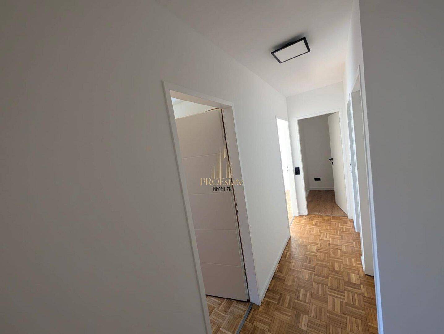 Heller Flur mit Parkettboden und weißen Wänden, der zu weiteren Räumen führt und einen einladenden Eingangsbereich bildet.