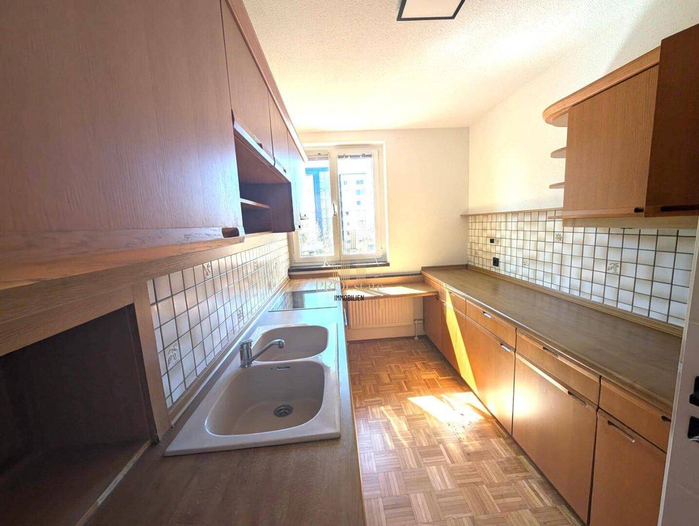 Helle Küche mit Holzschränken, Doppelspüle und Fenster mit Blick ins Freie, bietet viel Arbeitsfläche.