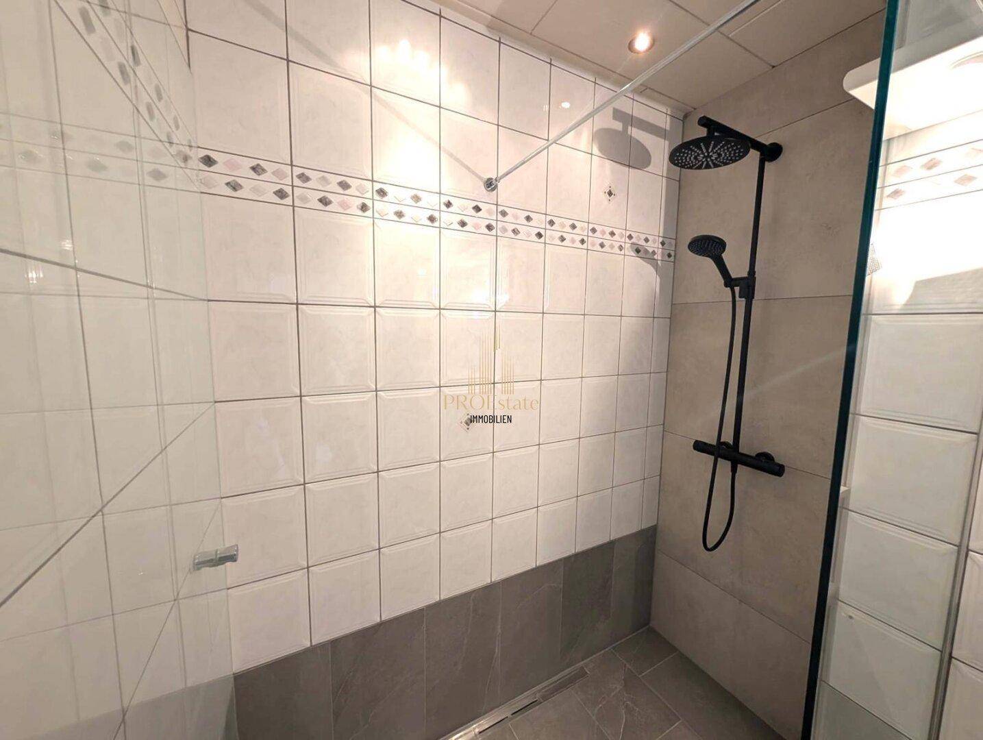 Moderne Duschkabine mit Regendusche und hellen Fliesen, die ein sauberes und zeitgemäßes Ambiente schafft.