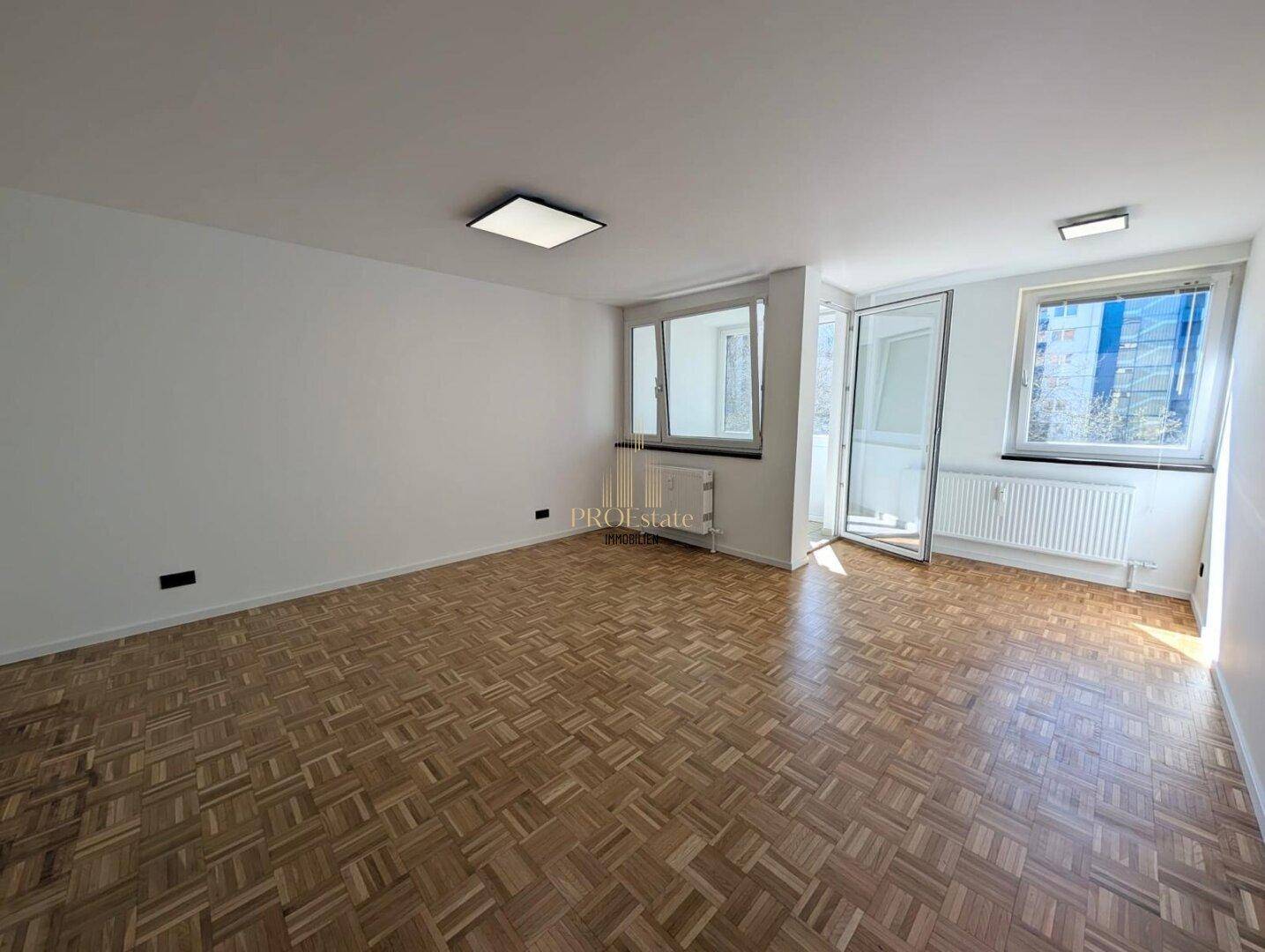 Lichtdurchflutetes Wohnzimmer mit Parkettboden, großen Fenstern und Zugang zum Balkon, ideal für entspannte Stunden.