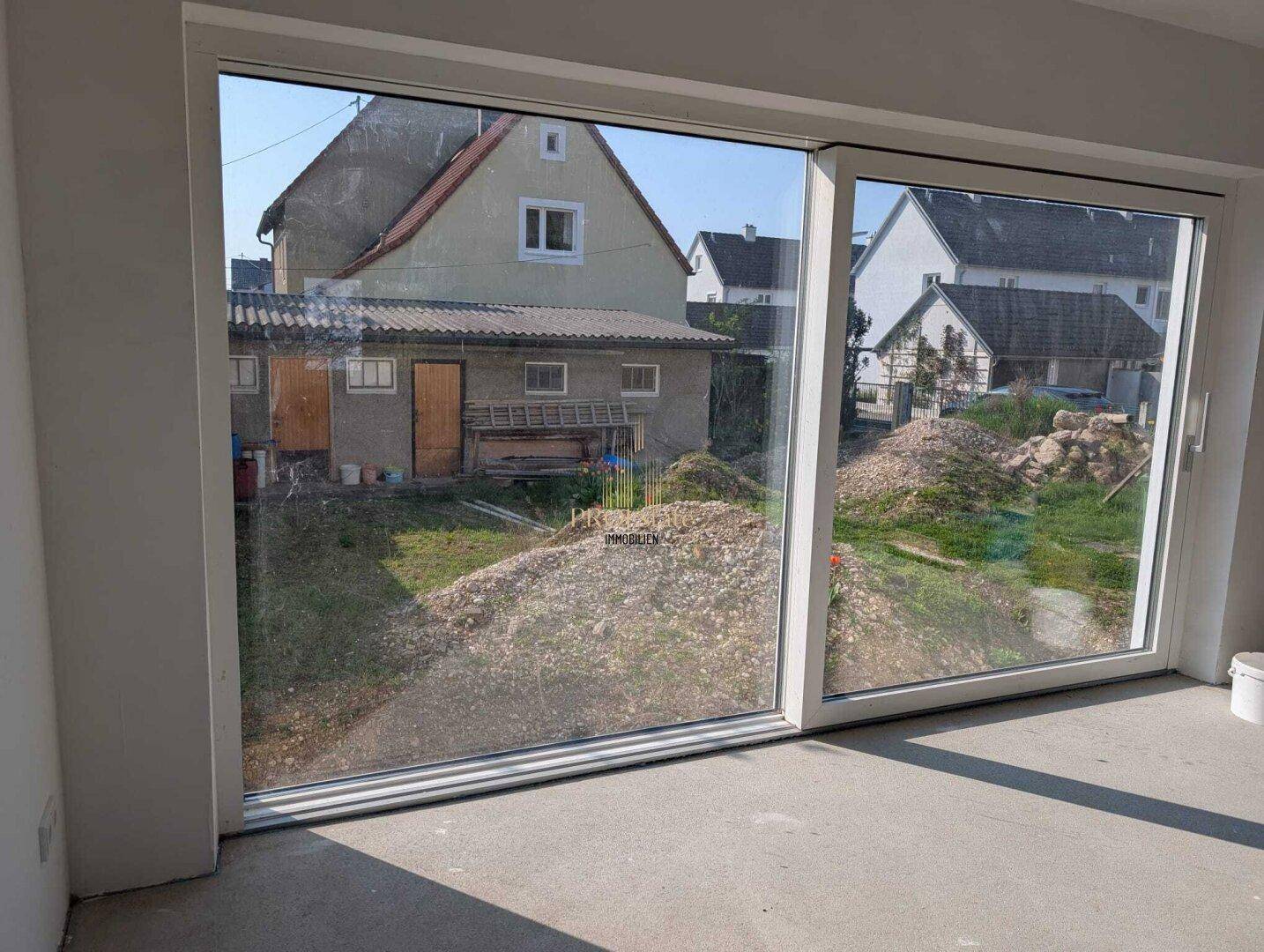 Große Fensterfront in einem unfertigen Raum mit Blick auf den Garten.