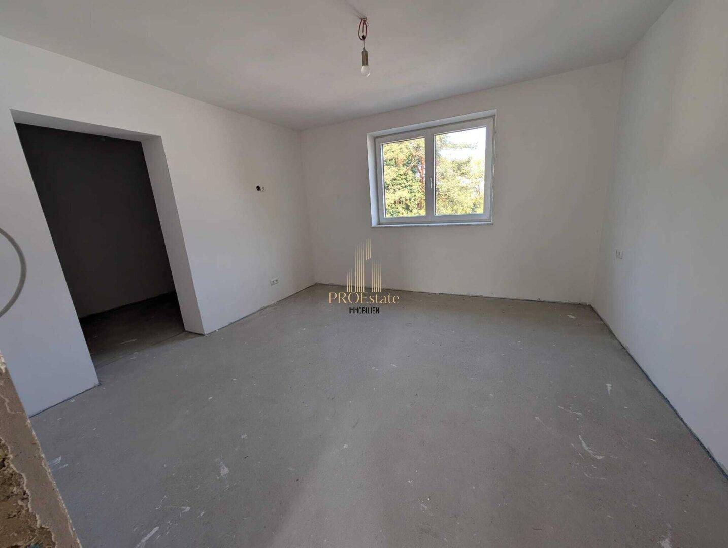 Leeres Schlafzimmer im Rohbauzustand mit Fenster und viel Tageslicht.