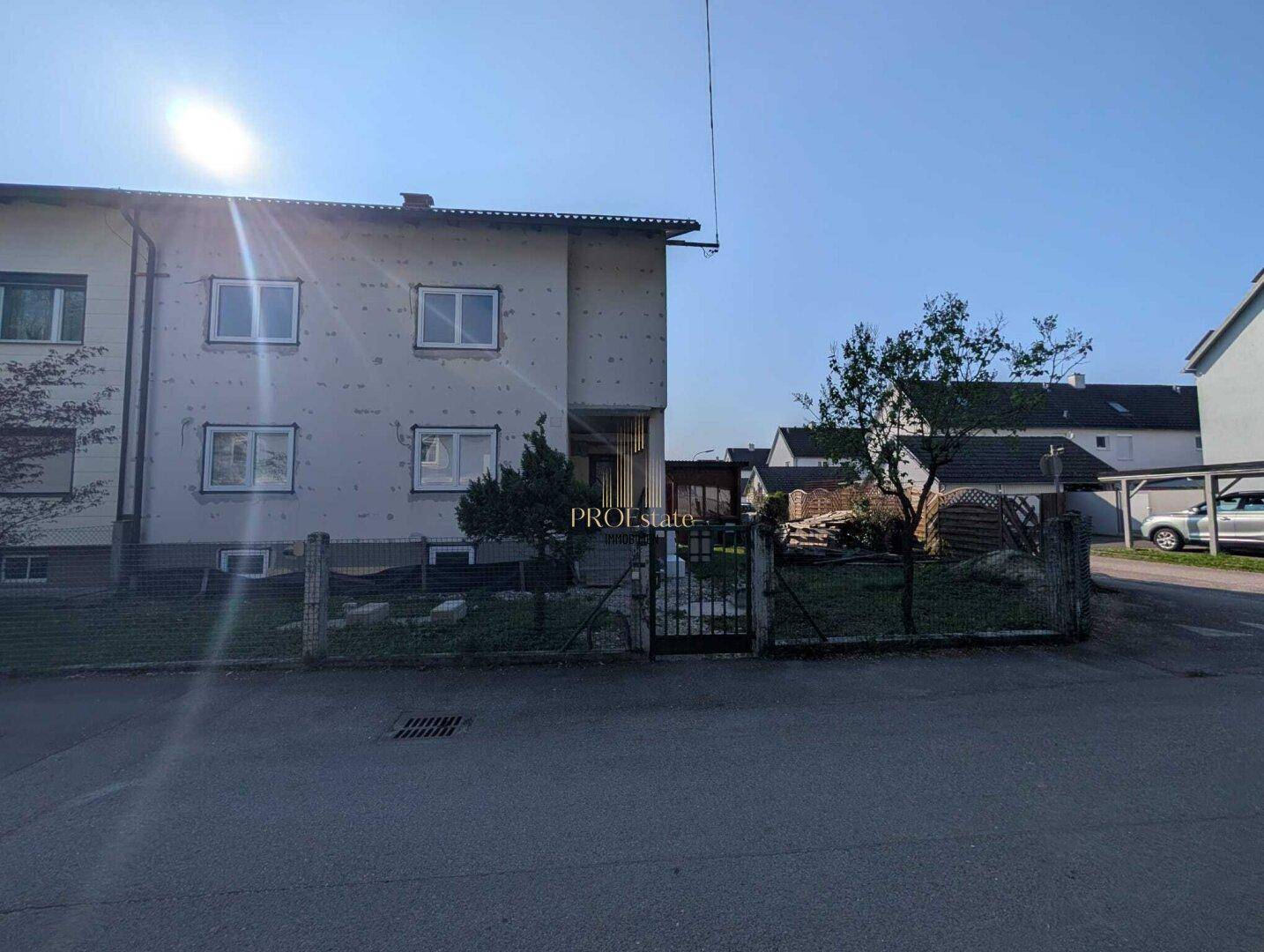 Ansicht des Wohnhauses von der Straße mit Zaun und Nachbargebäuden.
