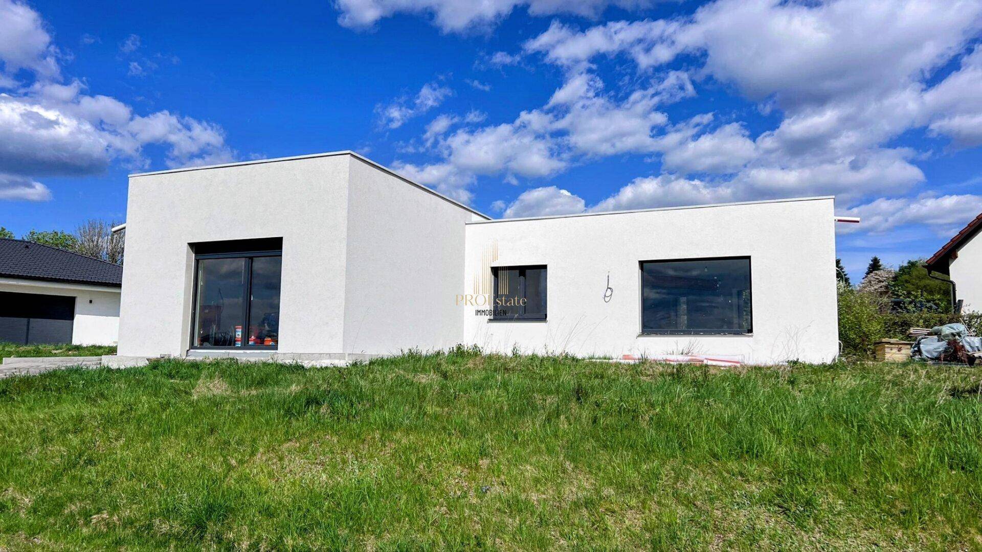 Modernes, weißes Einfamilienhaus mit Flachdach in Neubaugebiet, umgeben von Grünflächen.