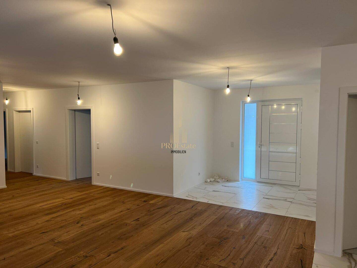 Unmöblierter Eingangsbereich mit Holzboden, Fliesen und heller Eingangstür.