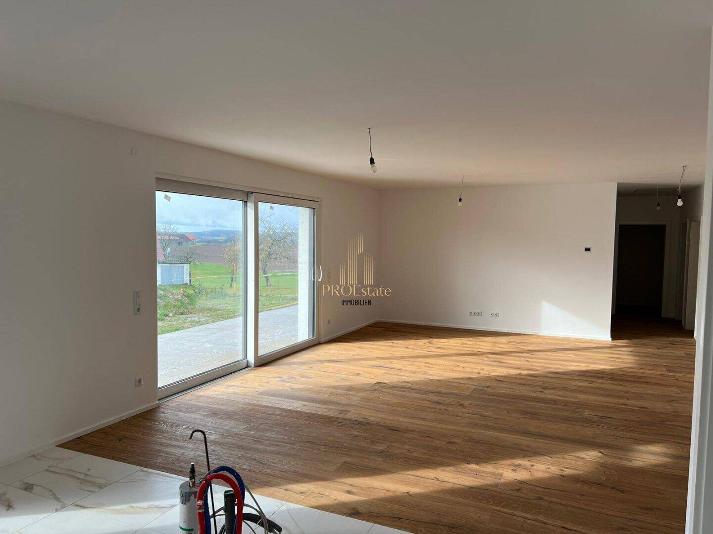 Geräumiger, unmöblierter Wohnbereich mit Holzboden und großen Schiebetüren zum Außenbereich.