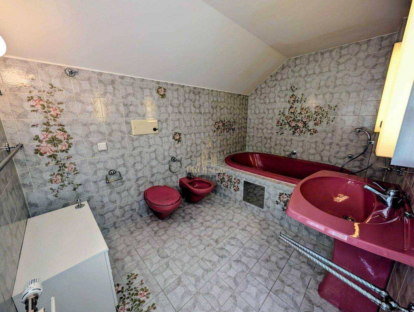 Badezimmer im 80er-Jahre-Stil mit rosa Sanitärobjekten und floral gemusterten Fliesen.
