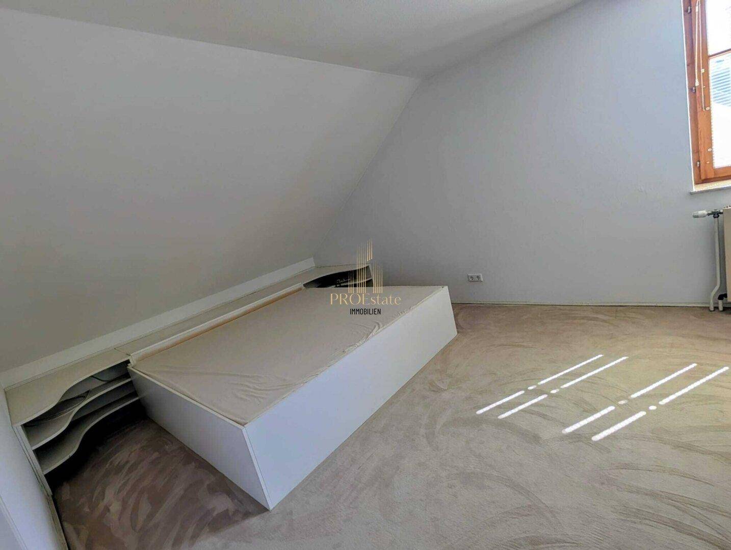 Gemütliches Schlafzimmer im Dachgeschoss mit schräger Decke, Teppichboden und integriertem Bett.