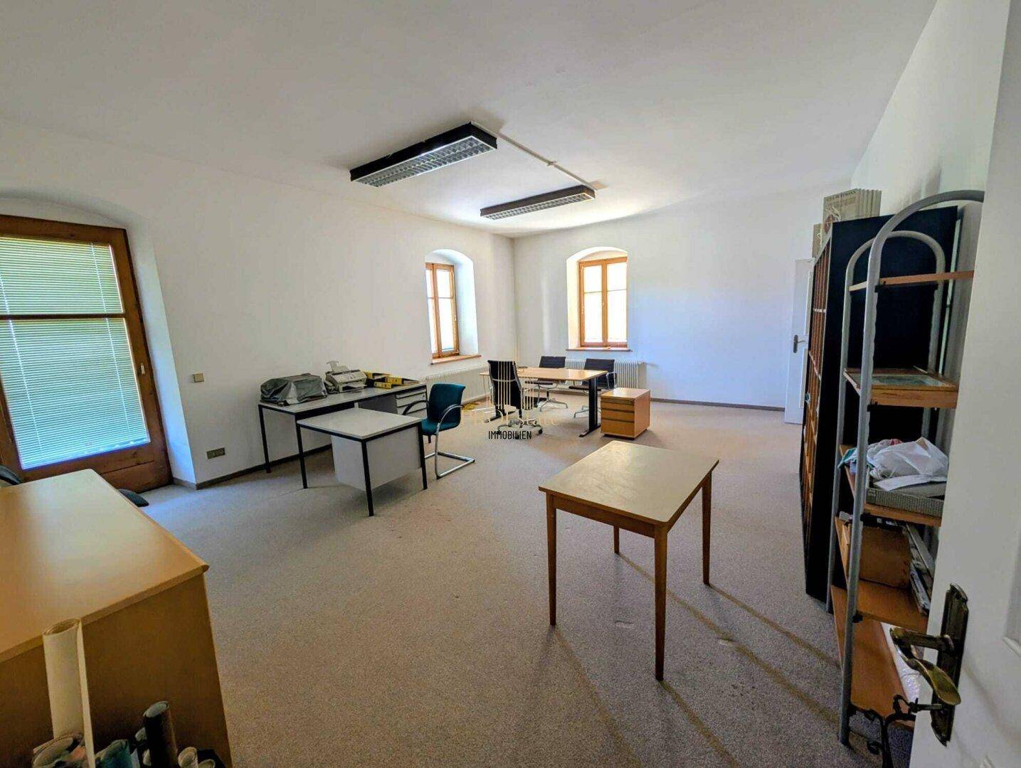 Großes Büro mit mehreren Arbeitsplätzen, Teppichboden und natürlichem Lichteinfall.