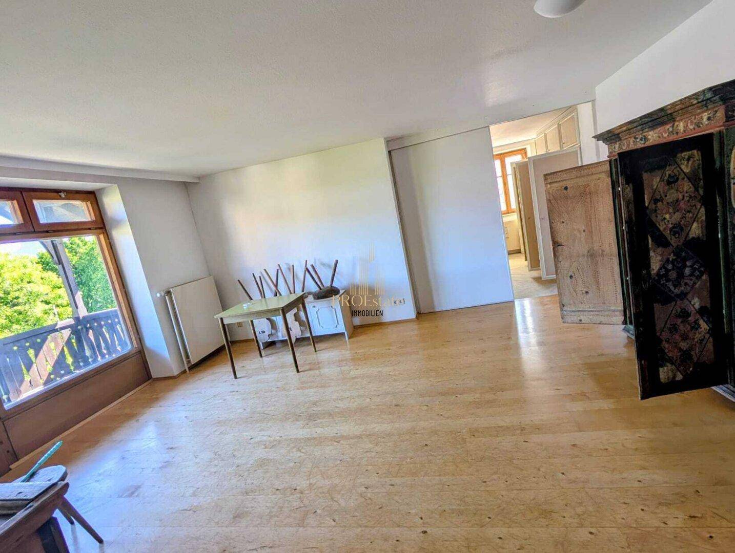 Heller Wohnbereich mit Holzboden und Zugang zu einem Balkon, der viel Tageslicht hereinlässt.