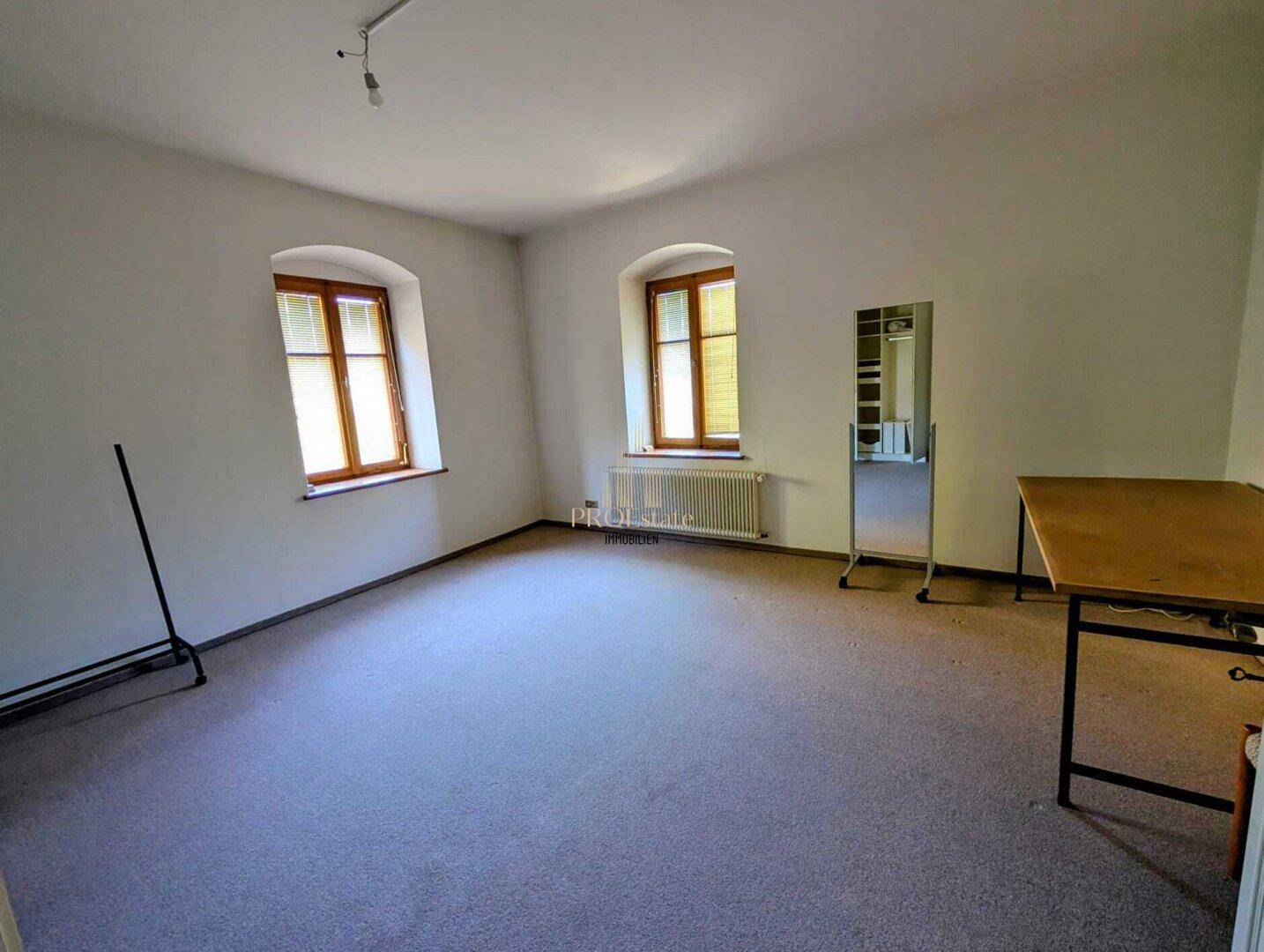 Leerer Raum mit Teppichboden und zwei Fenstern, bereit zur individuellen Gestaltung.