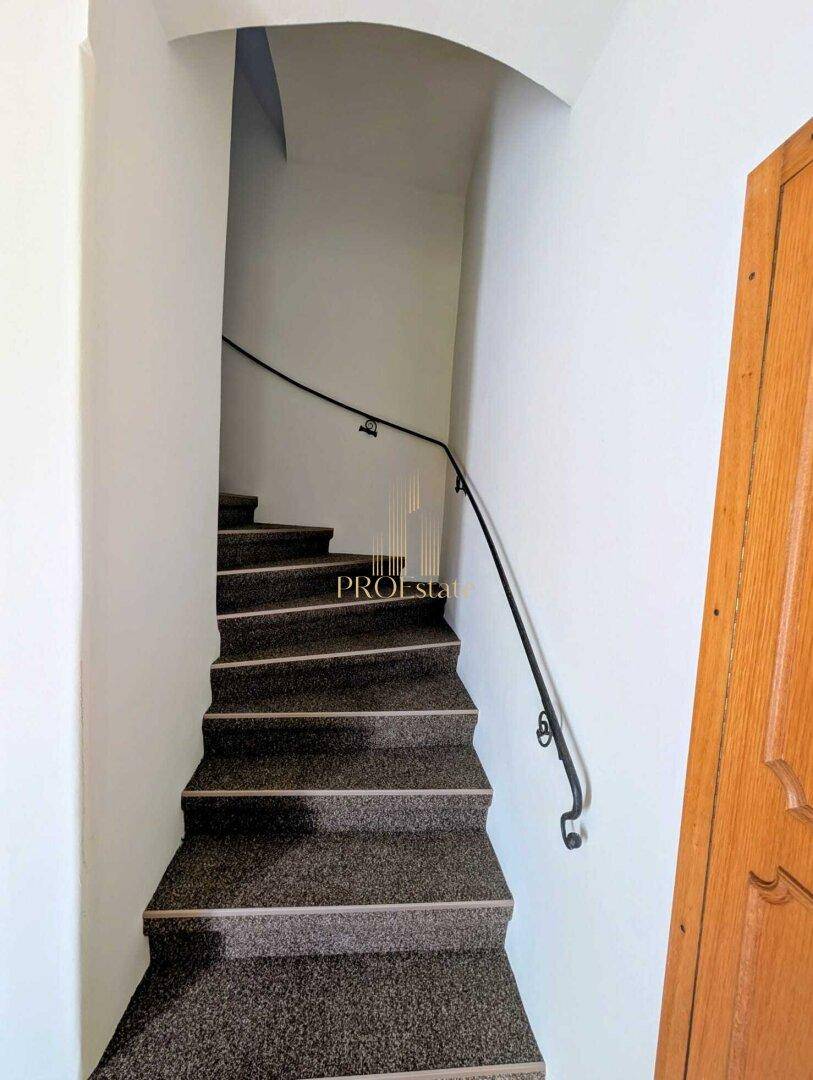 Treppenhaus mit dunklem Teppichboden und elegantem schwarzen Metallgeländer.