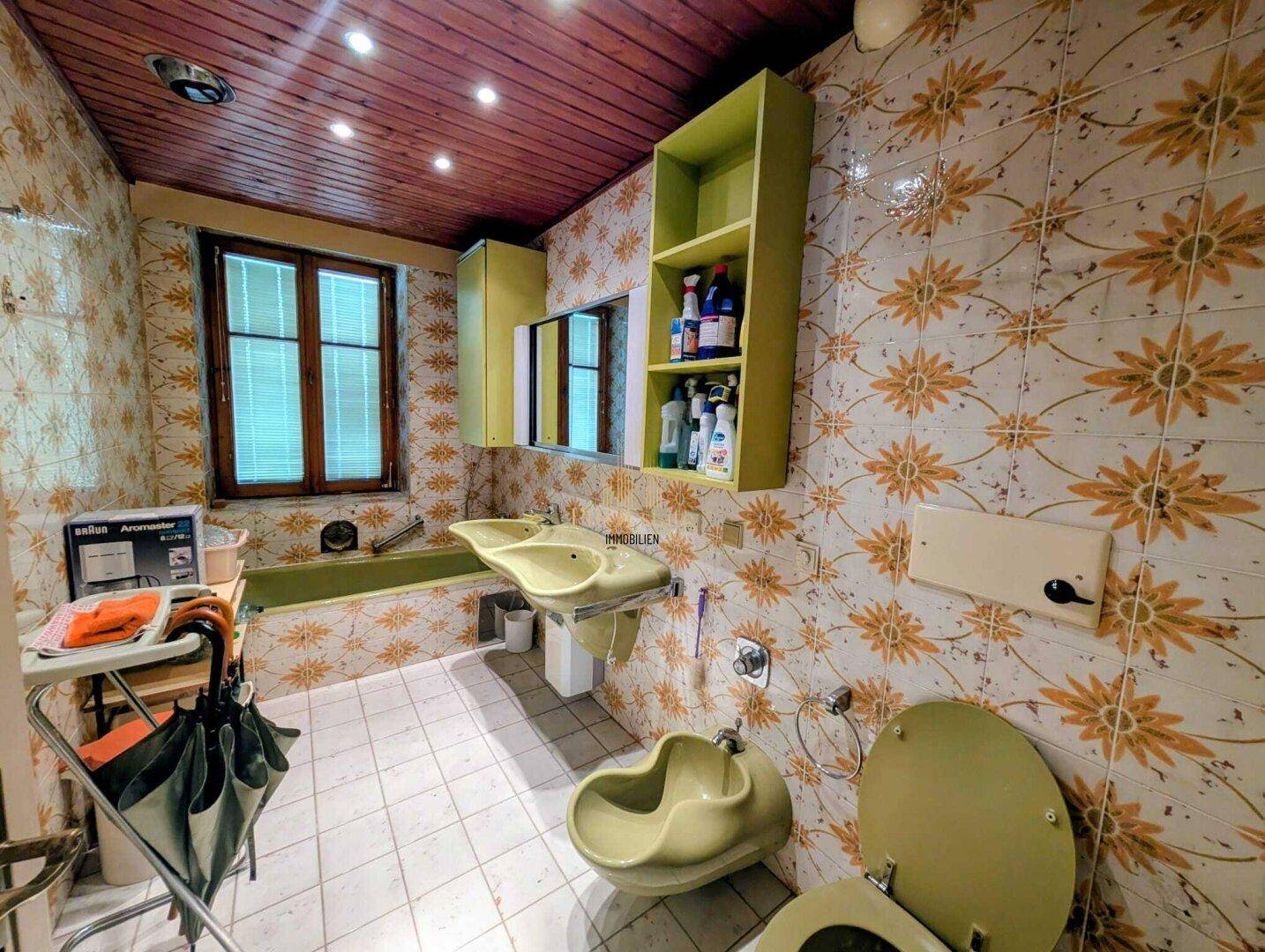 Badezimmer im Retro-Stil mit gelb-grünen Sanitärobjekten, gemusterten Fliesen und Holzdecke.
