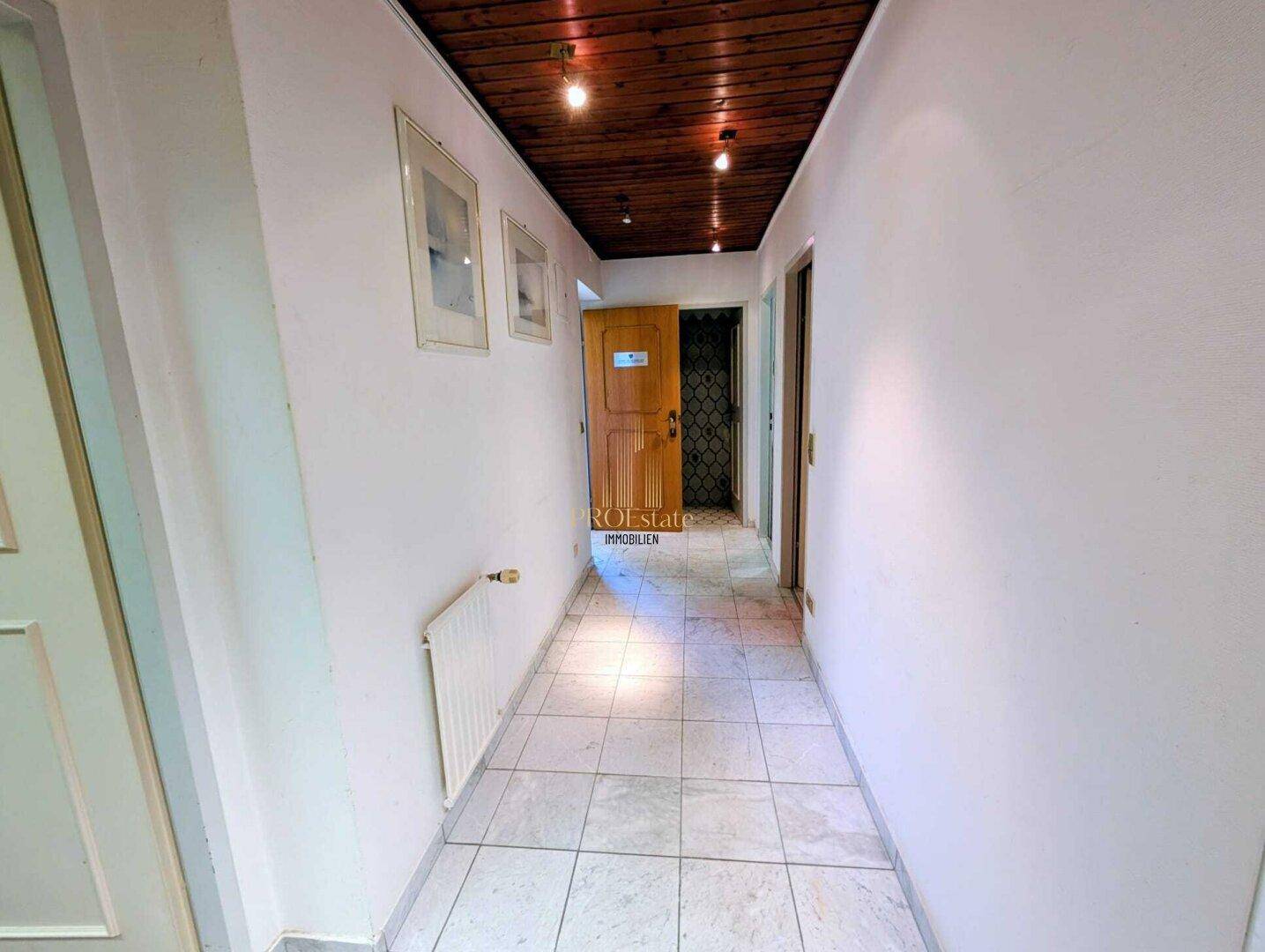 Heller Flur mit Fliesenboden, weißen Wänden und einer warmen Holzdecke.