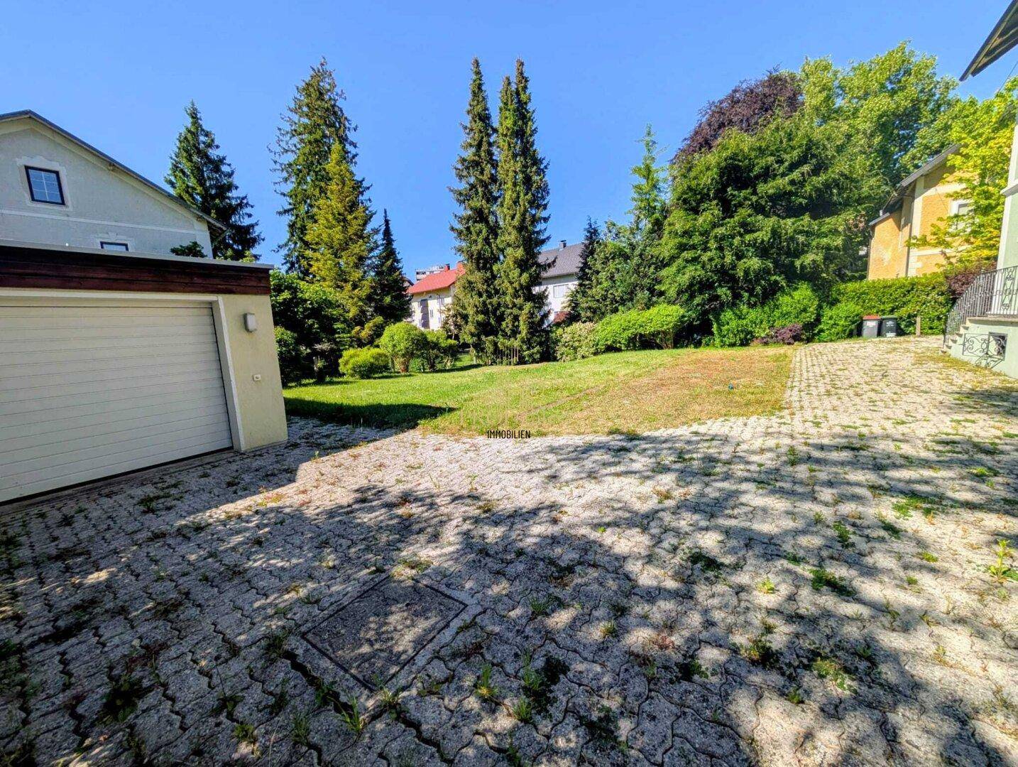 Einfahrt zur Garage mit gepflastertem Bereich und angrenzender Rasenfläche.