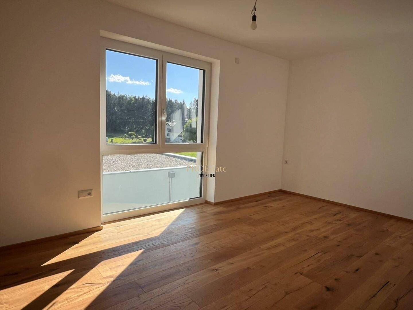 Helles Schlafzimmer mit Holzdielenboden und großem Fenster mit Blick ins Grüne.