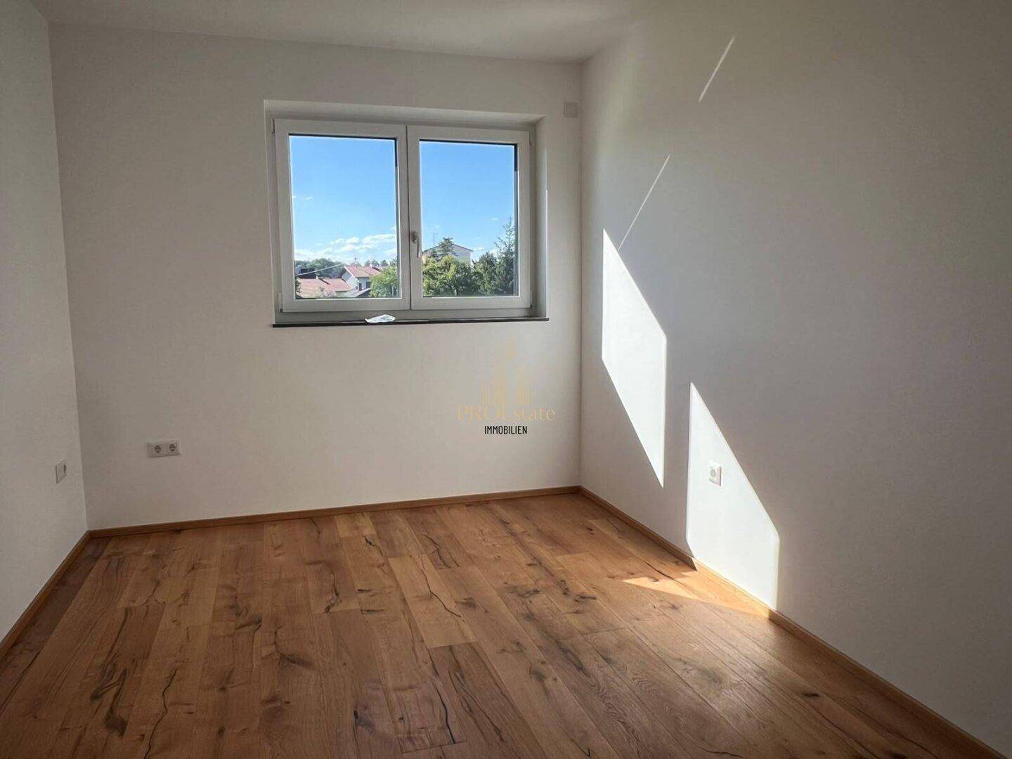 Geräumiges Schlafzimmer mit Holzdielenboden und Fenster, das viel Sonnenlicht hereinlässt.