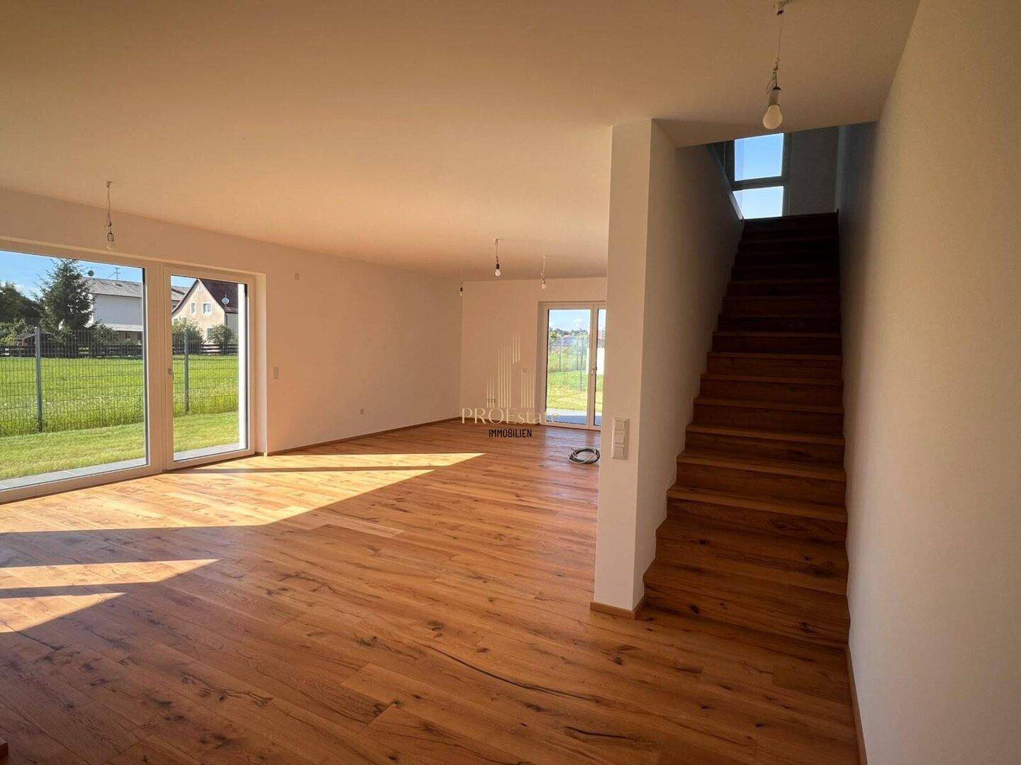 Offener Wohnbereich mit Holzdielenboden, viel Tageslicht und einer Holztreppe ins Obergeschoss.
