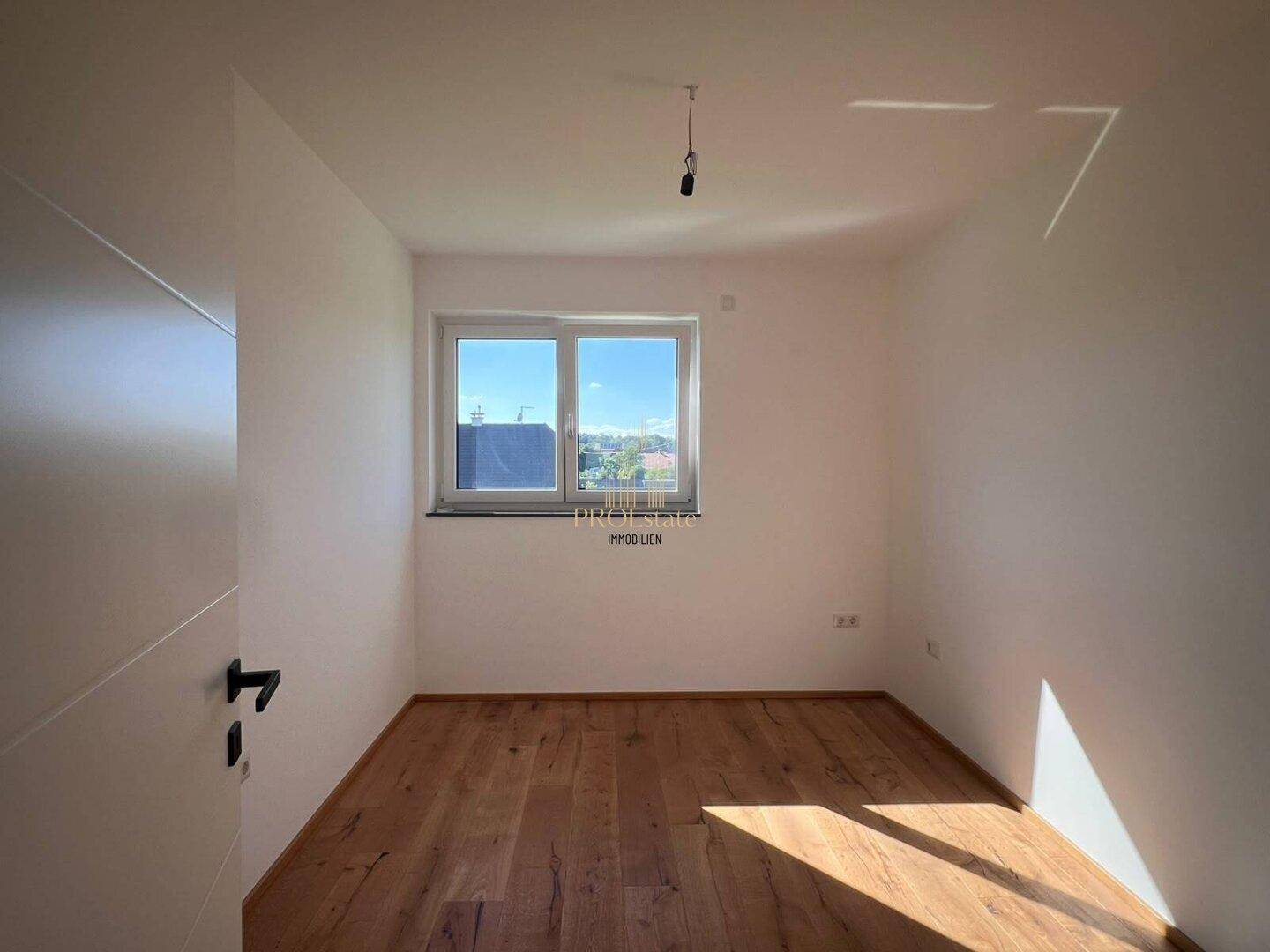 Helles Schlafzimmer mit Holzdielenboden und Fenster, das viel Sonnenlicht hereinlässt.