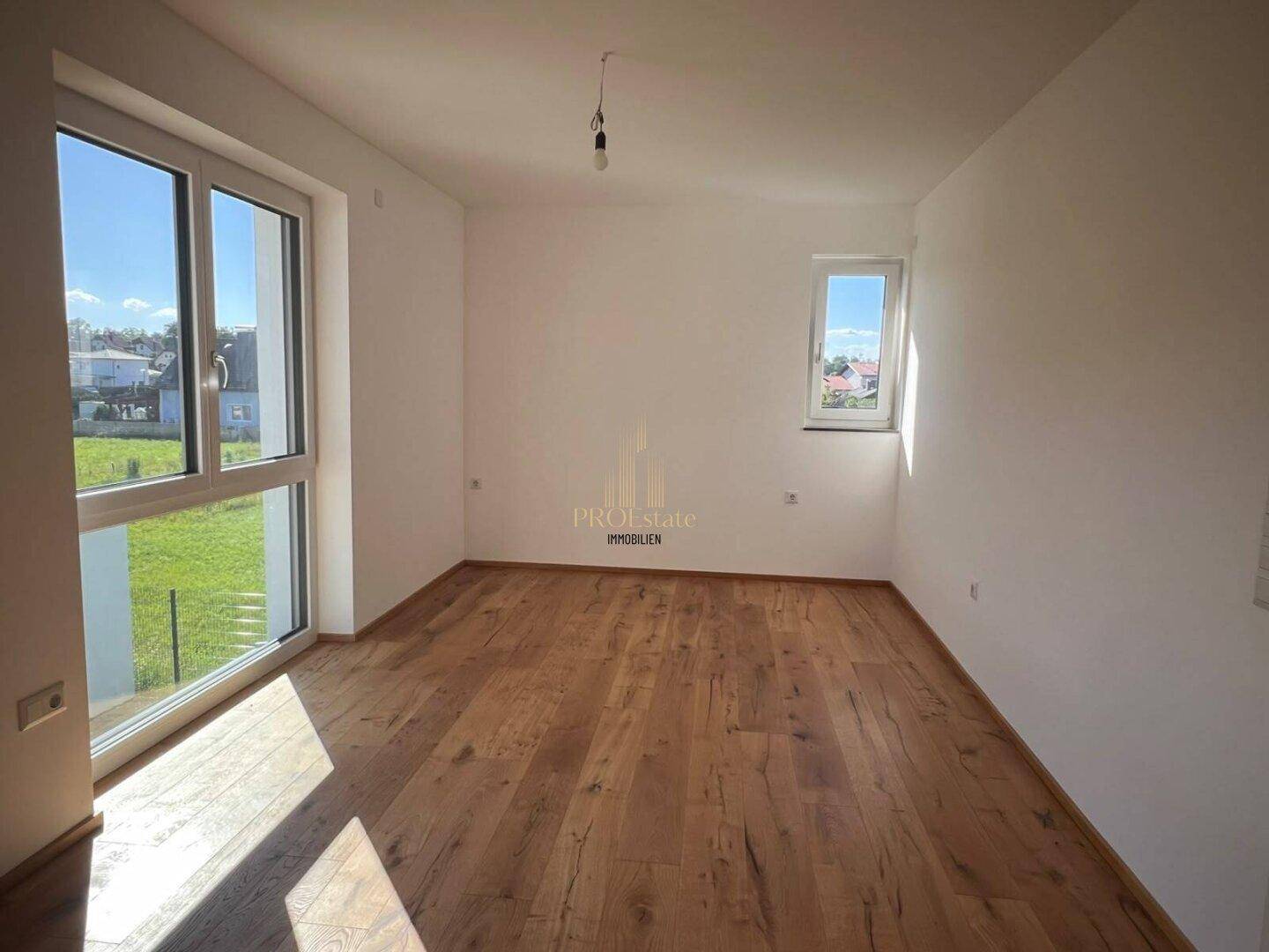 Schlafzimmer mit hellem Holzboden, großen Fenstern und viel natürlichem Tageslicht.
